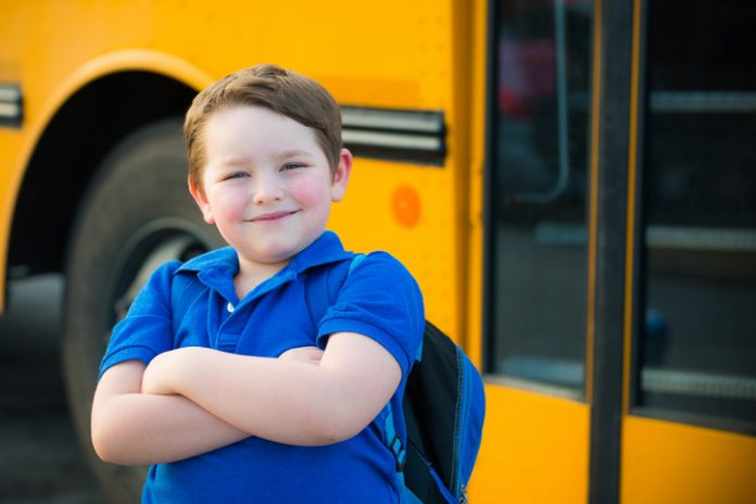 Happy young boy in front of school bus going back to school