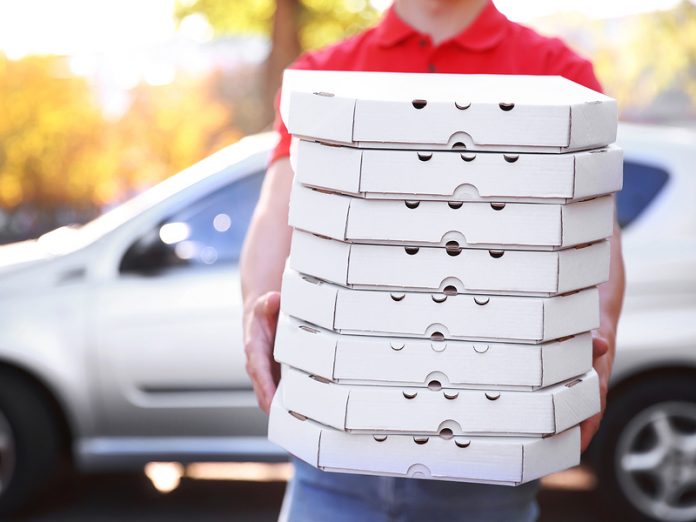 Pizza delivery boy holding boxes with pizza near car